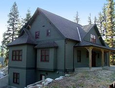 a large gray house sitting on top of a hill next to pine trees and rocks