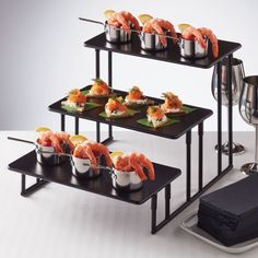 three tiered serving trays with shrimp and sushi on them next to wine glasses