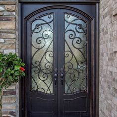 a black double door with decorative glass and brick wall in front of the entrance to a home