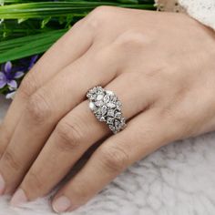 a woman's hand with a diamond ring on her finger and flowers in the background