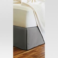 a bed with white and grey sheets on it's headboard, next to a wooden floor