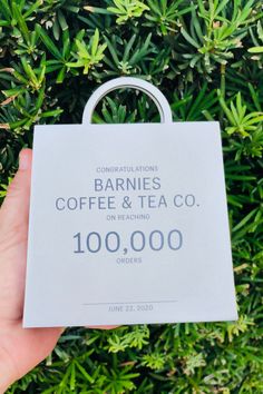 someone is holding up a coffee and tea bag in front of some green bushes with the words barnies coffee & tea co on it