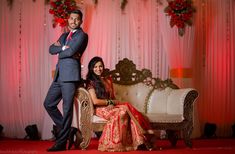 a man and woman sitting on a couch in front of a red wall with flowers