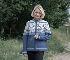 a woman in a blue and white sweater is standing on a dirt road near some trees