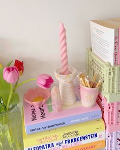 a stack of books with pink flowers in vases and other items on the table