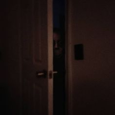 a person standing in front of a door with their face peeking through the doorway at night