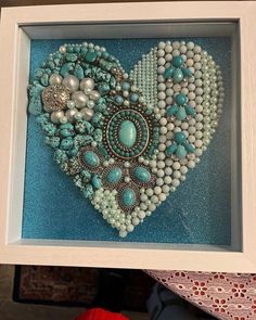 a heart made out of beads and other items in a white frame on top of a table