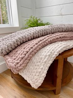 three blankets are stacked on top of each other in front of a wooden table with a potted plant