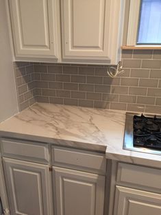 a kitchen with white cabinets and marble counter tops