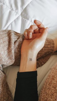 a woman's wrist tattoo with the letter h on her left hand, resting on a bed