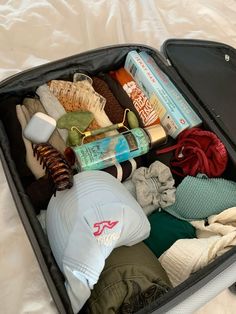 an open suitcase filled with clothing and other items on a white sheeted bed top