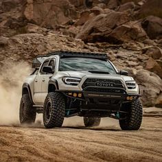 a white truck driving down a dirt road next to some rocks and trees in the background