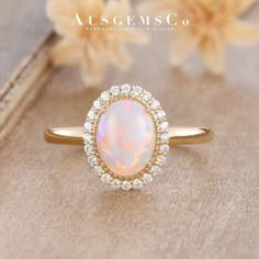 an opal and diamond ring sitting on top of a wooden table next to flowers