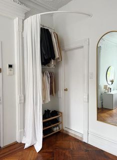 an open closet with clothes and shoes hanging on the door, next to a mirror