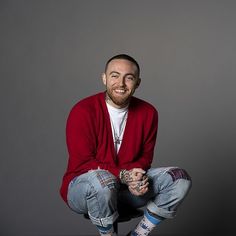 a man sitting on the ground with his legs crossed and wearing blue jeans, a red sweater and white sneakers