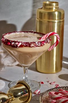 a drink in a glass with candy canes on the rim next to a gold shaker