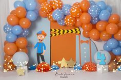 an orange and blue birthday party with balloons, decorations and paper cutouts on the wall