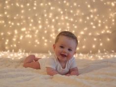 a baby laying on top of a bed next to a white wall with christmas lights