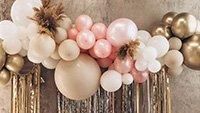 a bunch of balloons are attached to a wall with some gold and white decorations on it