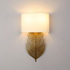 a wall light that has a white shade on the side and a gold leaf design