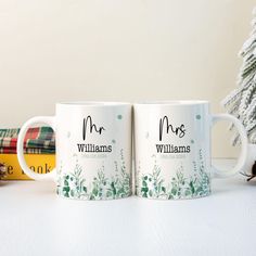 two personalized coffee mugs sitting next to each other on a table with a christmas tree in the background