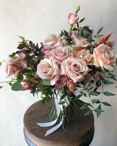 a vase filled with lots of pink flowers on top of a wooden table next to a wall