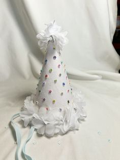 a small white party hat with colorful beads and bows on the top, sitting on a bed