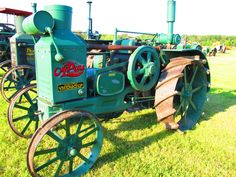 an old green tractor sitting on top of a grass covered field next to other farm equipment