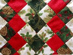 a quilted christmas table topper with holly and pine cones on red, white and green squares