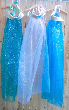 three dresses hanging on a clothes line with blue sequins and white ribbon tied to them