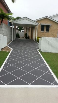 a driveway that has some grass in front of it and a white fence around it