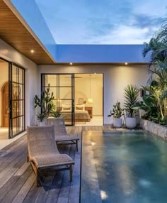 an outdoor swimming pool surrounded by greenery next to a patio with chairs and potted plants