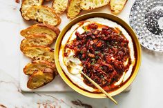 a bowl filled with food next to sliced bread on top of a white countertop