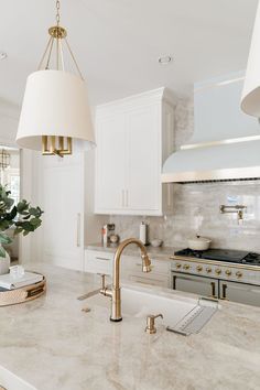 a white kitchen with marble counter tops and gold faucet light fixture over the sink