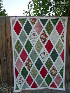 a quilt hanging on a wooden fence next to a tree with red, green and white squares