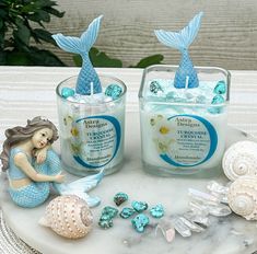 two mermaid candles sitting on top of a table next to shells and seashells