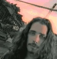 a man with long hair standing in front of a helicopter