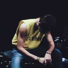 a man sitting on top of a motorcycle wearing a yellow t - shirt and blue jeans