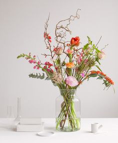 a vase filled with lots of flowers on top of a white table next to two glasses