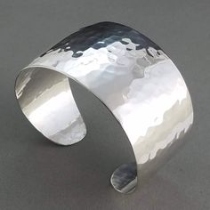 A 1.5 inch wide solid sterling silver cuff with silky smooth edges that tapers off to rounded ends. Given an elegant dome and a bright polish, the hammered facets on this cuff have a watery effect and can reflect light to your surroundings. Eye catching when worn on a night out. Particularly dazzling in sunlight, reflections sparkle like glittering points of light dancing on sunlit waves. Hand cut, formed and hammered by me from solid sterling silver sheet. Stamped STERLING inside with my spiral cat logo. Your personal cuff will be made to fit your wrist so will look similar to photo. Last two photos show where on wrist to take a snug measurement. Descriptive information about example cuff in photo: - 38 grams and slightly springy. - Inside length of oval cuff measures 5.6" with a 0.75" op Genuine Turquoise Jewelry, Hot Jewelry, Sterling Bracelets, Turquoise Bracelet Cuff, Ball Bracelet, Turquoise Cuff, Bracelet Cuff, Hammered Silver, Sterling Silver Cuff