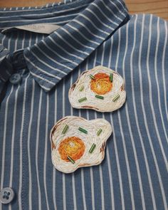 two pins are attached to a blue shirt with white and orange flowers on the front