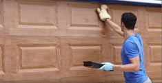 a man in blue shirt and gloves painting a wooden garage door