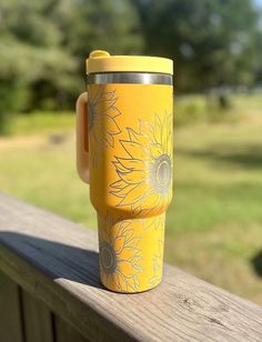 a yellow coffee cup with sunflowers painted on it sitting on a wooden railing