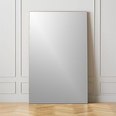 an empty mirror on the floor in front of a wall with white paneling and wooden floors