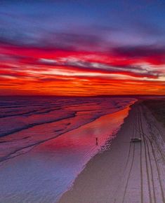 the sun is setting over the ocean and beach with tracks in the sand on the shore