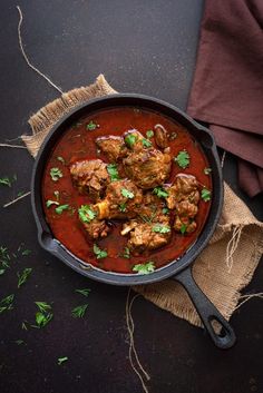 meatballs and tomato sauce in a skillet on a black surface with garnishes