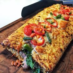 a pizza with tomatoes, spinach and other toppings on a cutting board