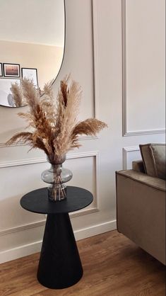 a vase filled with dried flowers on top of a black table next to a couch