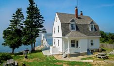 a white house sitting on top of a lush green field next to the ocean with a lighthouse in the background