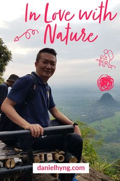 a man sitting on top of a wooden bench next to a lush green hillside with mountains in the background